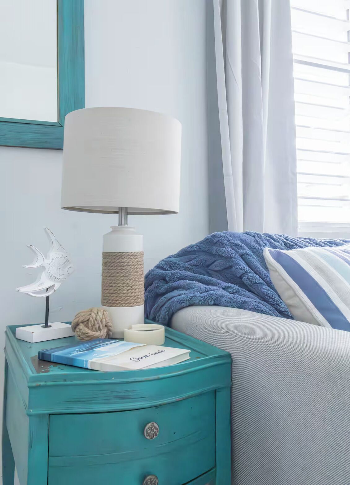 A teal bedside table with a lamp, a decorative fish sculpture, and a book.