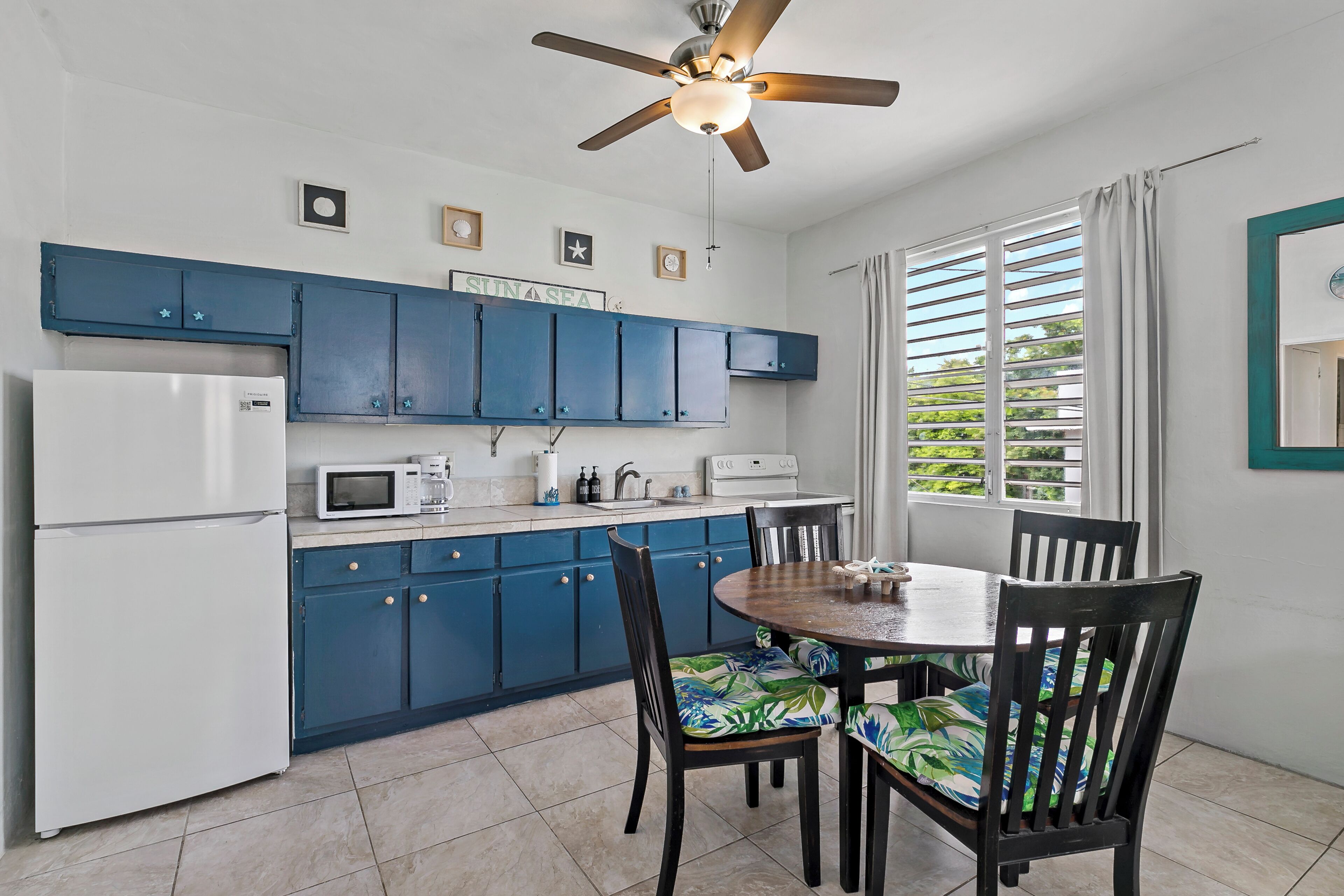 A kitchen with blue cabinets, a white refrigerator, a microwave, and a ceiling fan.