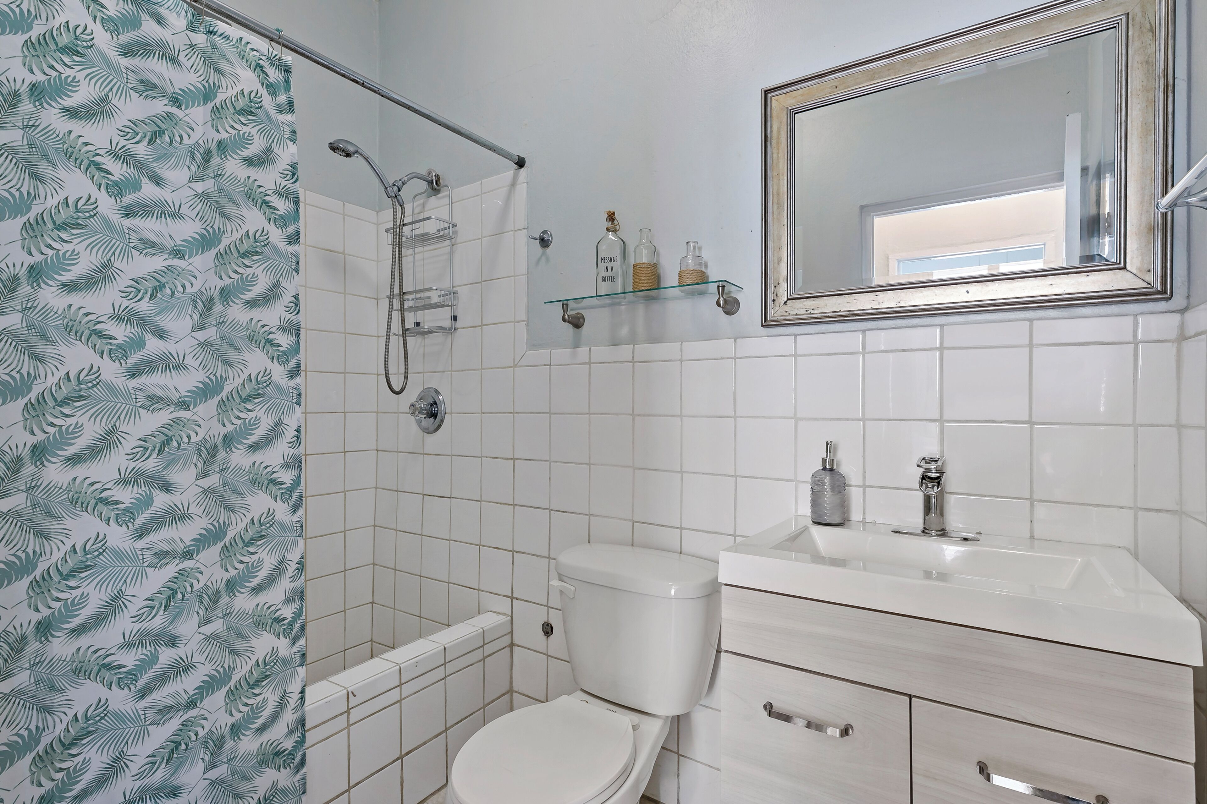 A bathroom with a toilet, a shower, a sink, and a mirror.