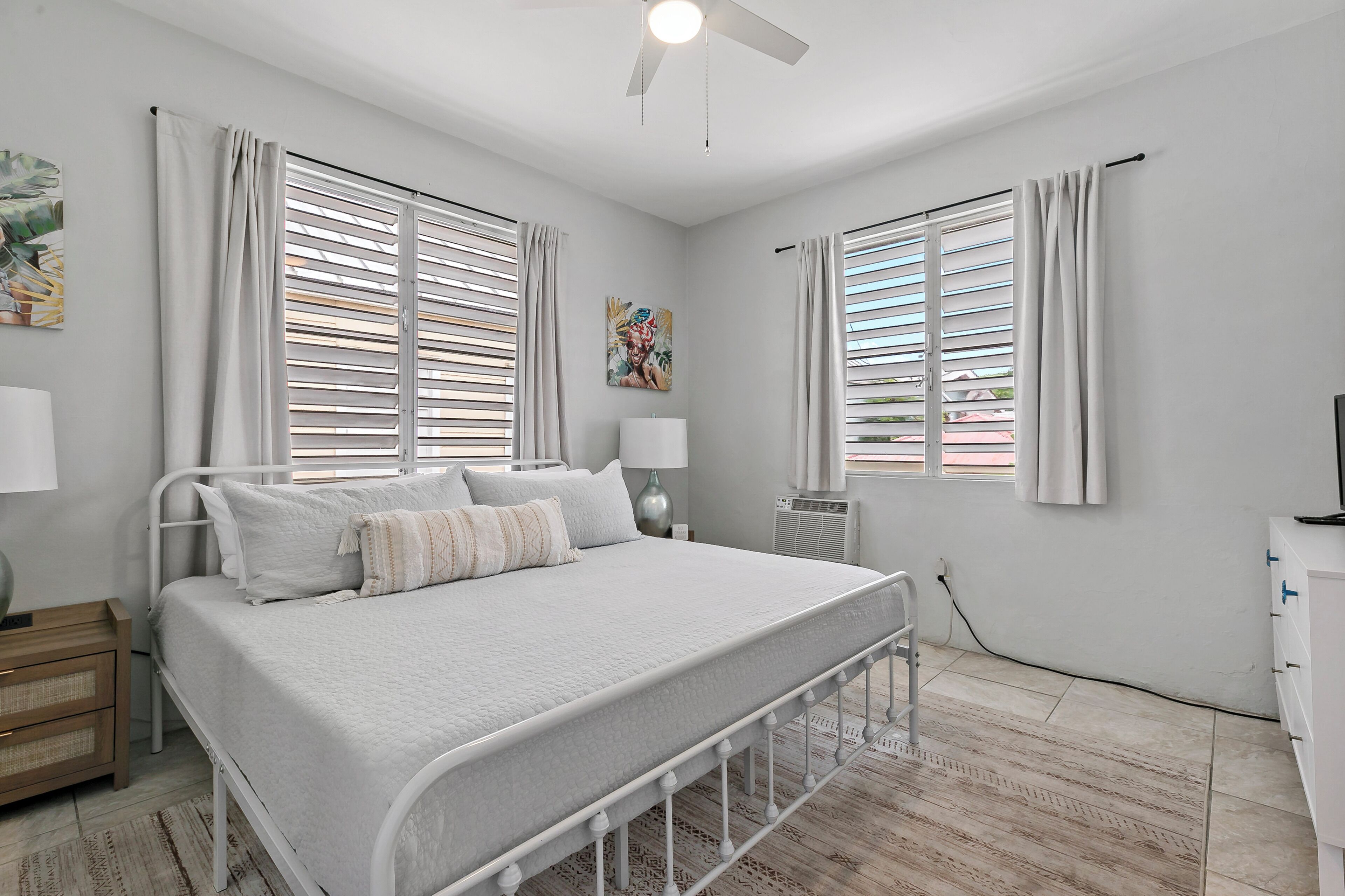 Un dormitorio con cama, lámparas de noche, ventilador de techo y una ventana con persianas.