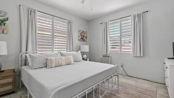Un dormitorio con cama, lámparas de noche, ventilador de techo y una ventana con persianas.