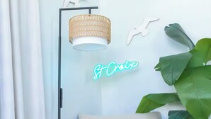 Ein modernes Wohnzimmer mit einem beigefarbenen Sofa, einem kleinen runden Tisch mit Pflanze, einer Stehlampe und einem Neon-Leuchtschild.