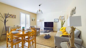 A living room with a dining area, a sofa, a TV, and a lamp. - House with garden, terrace & pétanque - 6 guests (Saint-Hilaire-de-Riez)