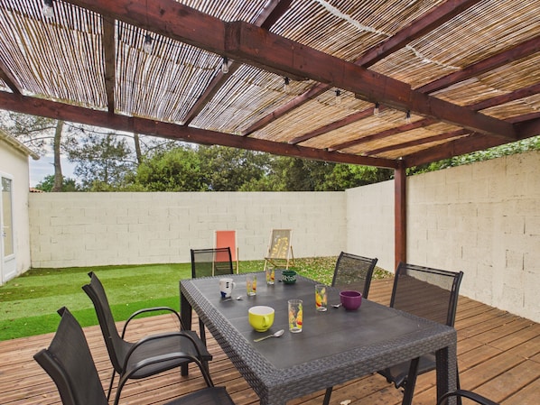 An outdoor patio with a table and chairs, a pergola overhead, and a white brick wall in the background.