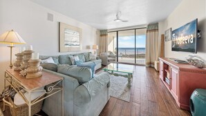 Un salon spacieux avec un canapé, une table basse en verre, un téléviseur et un balcon offrant une vue agréable.