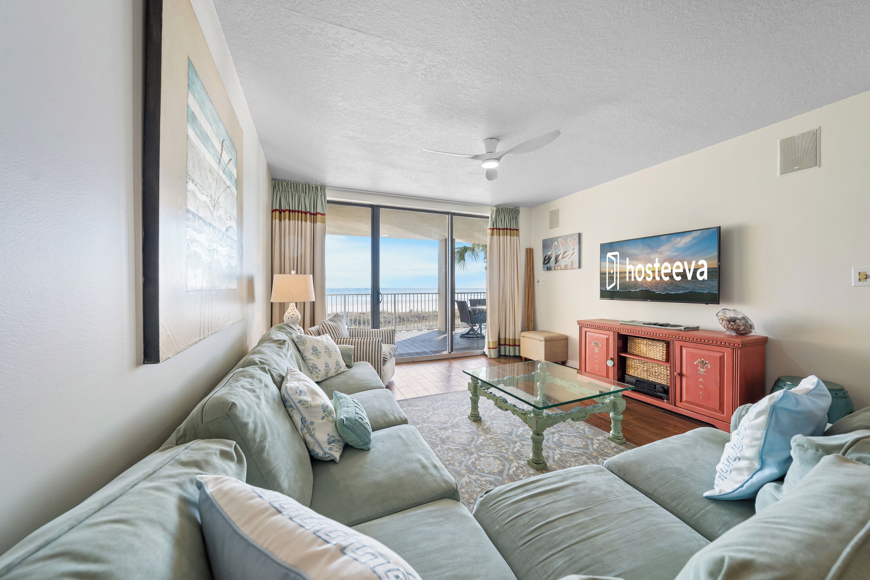 A spacious living room with a large sofa set, a glass coffee table, and a television mounted on the wall.