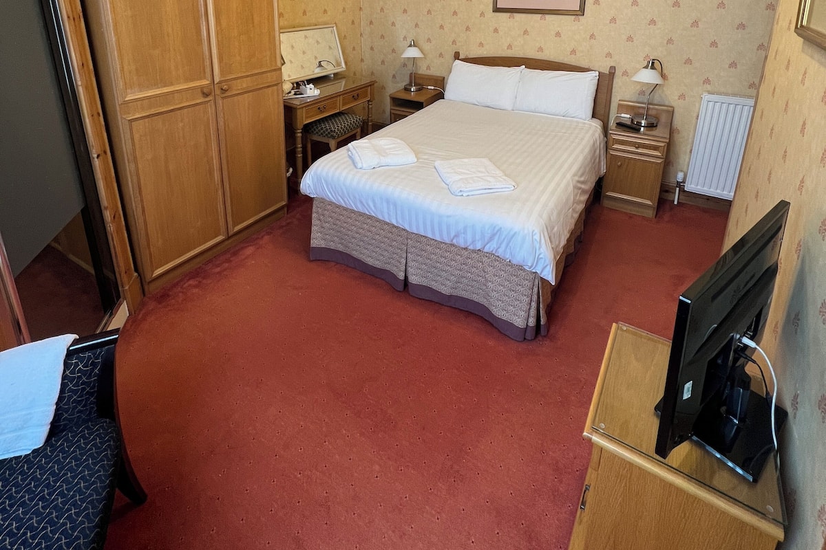 A hotel room with a bed, two bedside tables, a wardrobe, a desk, and a television.