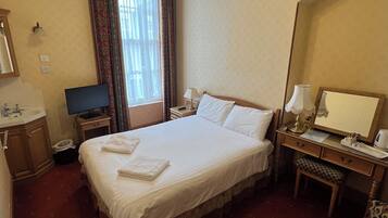 A hotel room with a large bed, a desk with a lamp, a television, and a mirror.