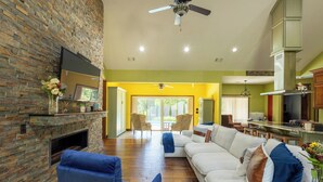 A living room with a fireplace, a sofa, a blue armchair, and a kitchen area in the background.