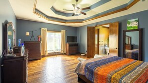 A spacious bedroom with a large bed, wooden dresser, and a ceiling fan.