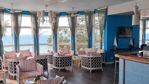 A room with striped chairs, a bar area, and large windows with curtains. - Dona Ana Hotel (Vilanculos)