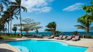 A swimming pool with lounge chairs, palm trees, and a view of the ocean. - Dona Ana Hotel (Vilanculos)