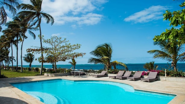 A swimming pool with lounge chairs, palm trees, and a view of the ocean. - Dona Ana Hotel (Vilanculos)