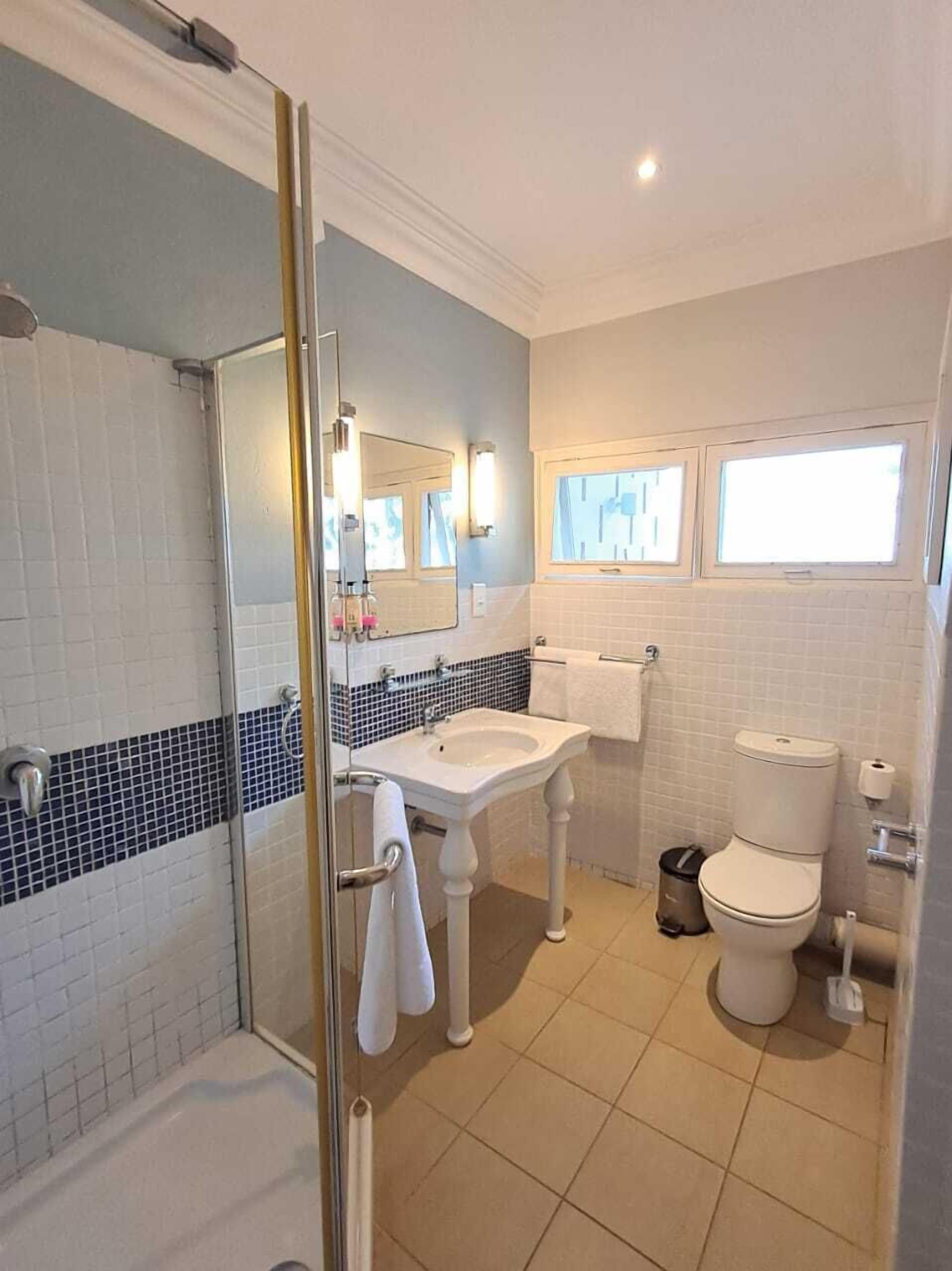 A bathroom with a glass shower enclosure, a white sink, a toilet, and a window.