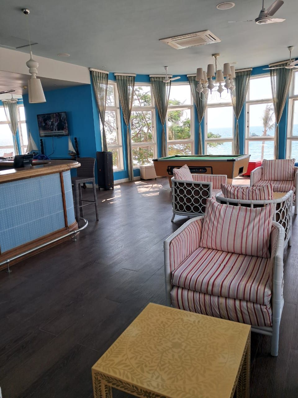 Una habitación con mesa de billar, sillas a rayas, zona de bar y amplias ventanas con cortinas.