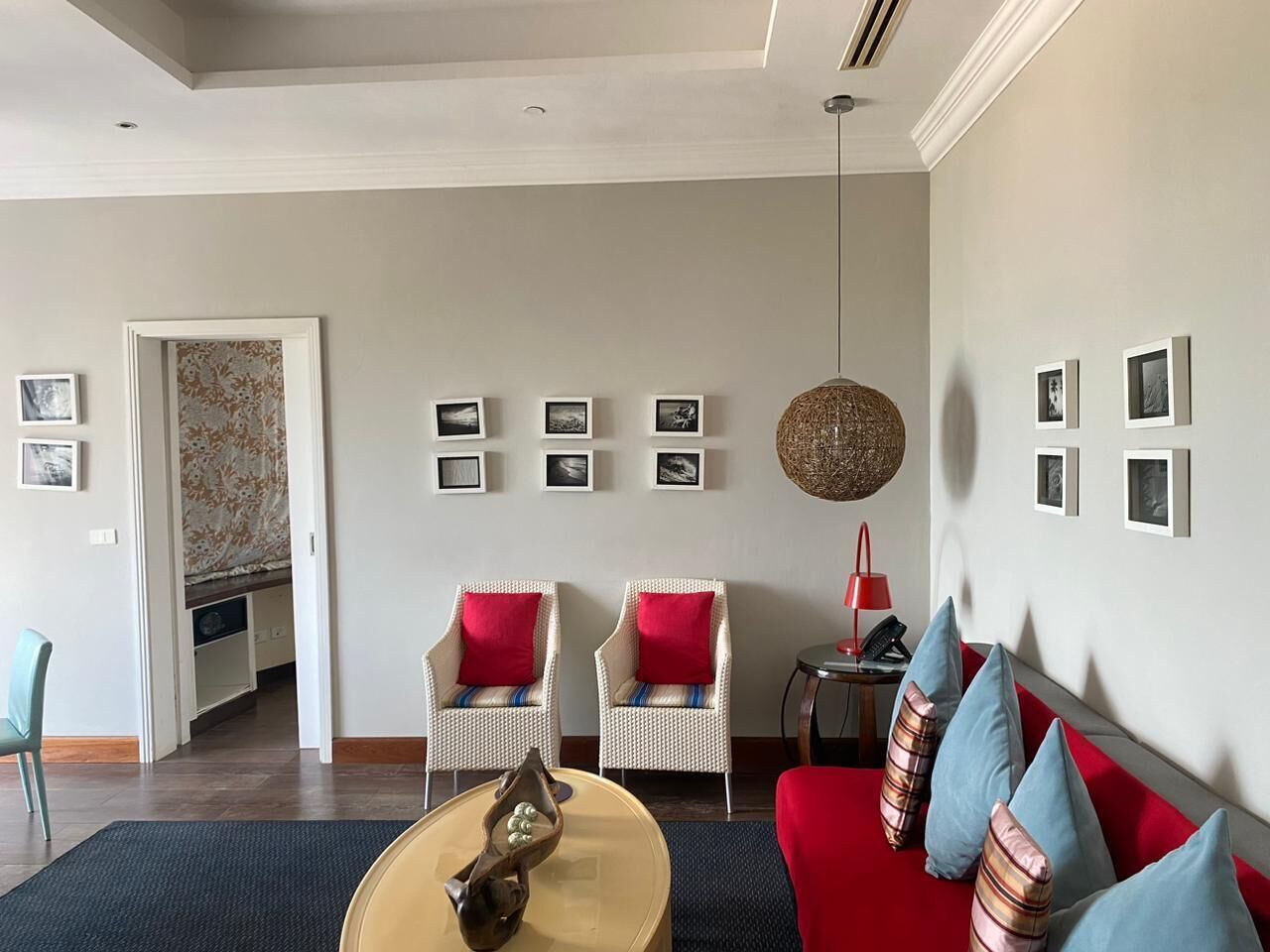 Un salon moderne avec un canapé rouge, deux fauteuils en osier avec des coussins rouges, une table basse et un luminaire suspendu.