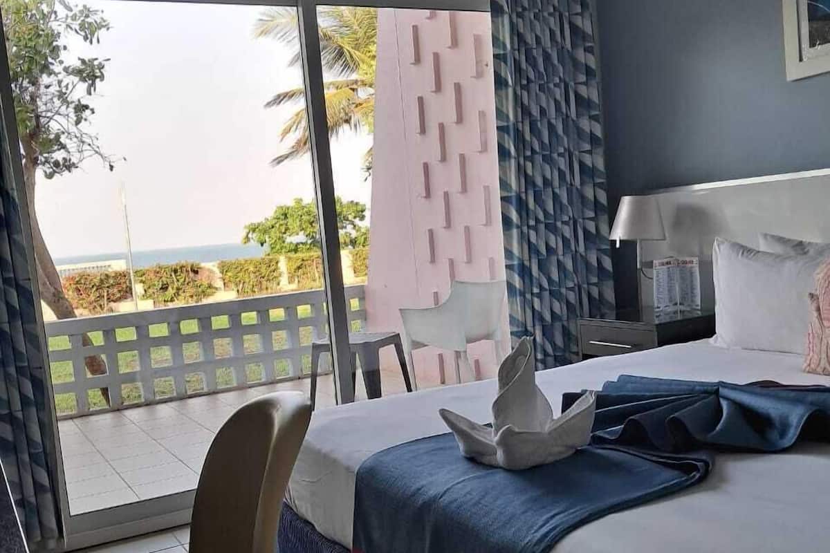Ein Hotelzimmer mit Bett, Sessel, Nachttisch und Blick ins Freie.