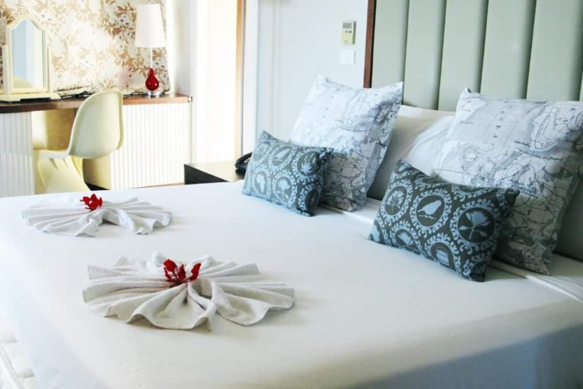 Ein ordentlich bezogenes Bett mit gemusterten Kissen und einem Handtuch mit roter Blume.