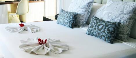 A neatly made bed with patterned pillows and a towel with a red flower.