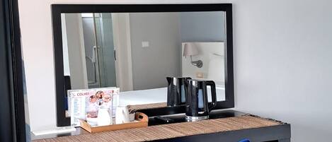 Una habitación con escritorio, silla, televisor montado sobre el escritorio y un espejo que refleja la habitación.