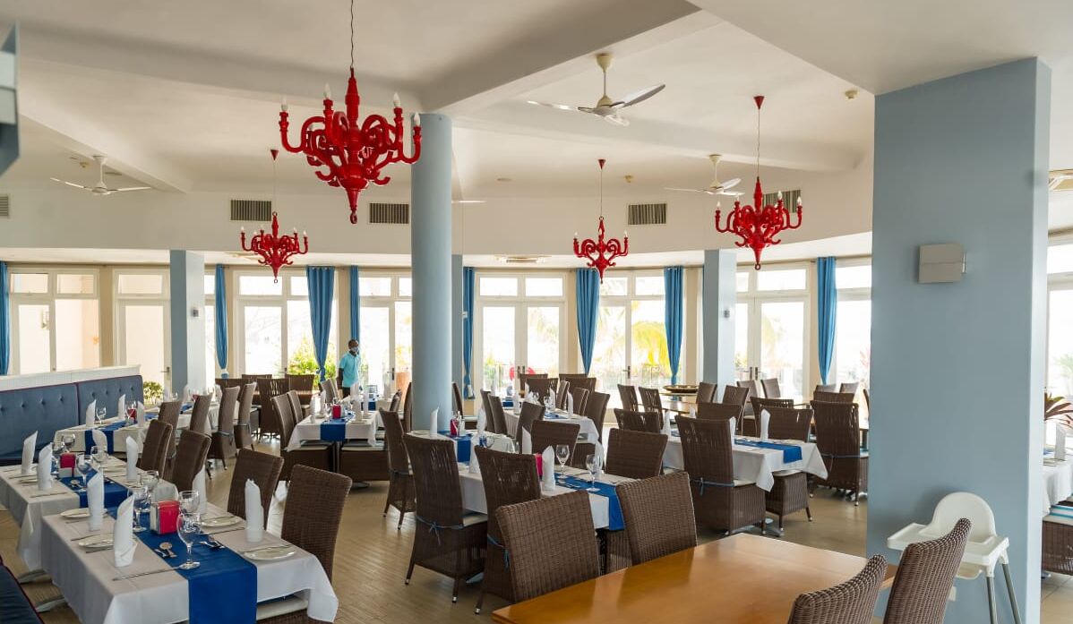 Un comedor amplio con varias mesas y sillas, candelabros rojos y ventanas grandes que dejan entrar luz natural.