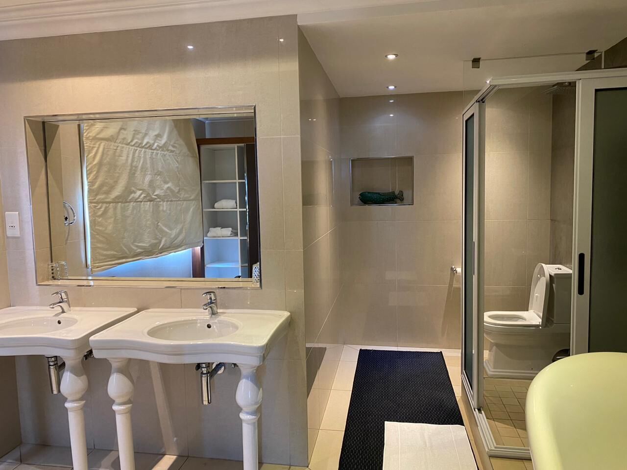 A bathroom with two sinks, a large mirror, a shower area, and a toilet.