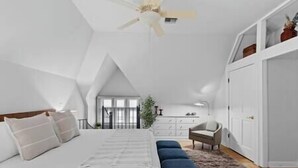 A bedroom with a large bed, a ceiling fan, a dresser, and a view of the outdoors.