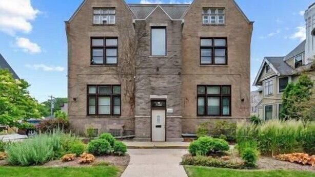 A two-story stone building with a central entrance, symmetrical windows, and a small porch area.