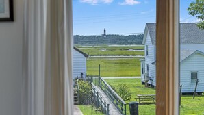 A view from a window overlooking a rural landscape with a lighthouse, grassy fields, and white houses. - The Virginia Lee by Seaside Vacations & Sales (Chincoteague Island)