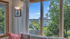A cozy living room with a large window offering a view of a residential area, a lamp, and a cushion with a message. - The Virginia Lee by Seaside Vacations & Sales (Chincoteague Island)
