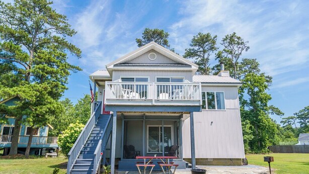 A two-story house with a balcony, a covered patio, and a staircase leading to the upper level. - The Virginia Lee by Seaside Vacations & Sales (Chincoteague Island)