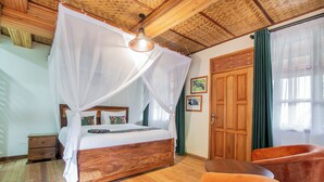 A wooden four-poster bed with a canopy, a wooden nightstand, a round wooden table, and two orange chairs. - Gorilla Leisure Lodge (Bugambira)