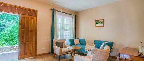 Ein Wohnzimmer mit Holzboden, einem blaugrünen Sofa, zwei Sesseln, einem kleinen runden Tisch und einem Holztisch mit einer Flasche.