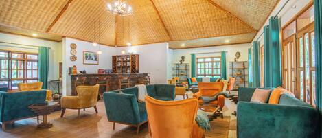 A spacious living area with a high, woven ceiling, wooden flooring, and a variety of seating options including teal and orange upholstered chairs and sofas.