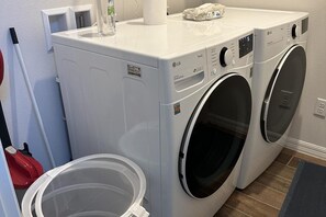 A laundry room with two white front-loading washing machines, a red vacuum cleaner, and a plastic laundry basket. - Bungalow Villa Close to Attractions and Amenities (Kissimmee)