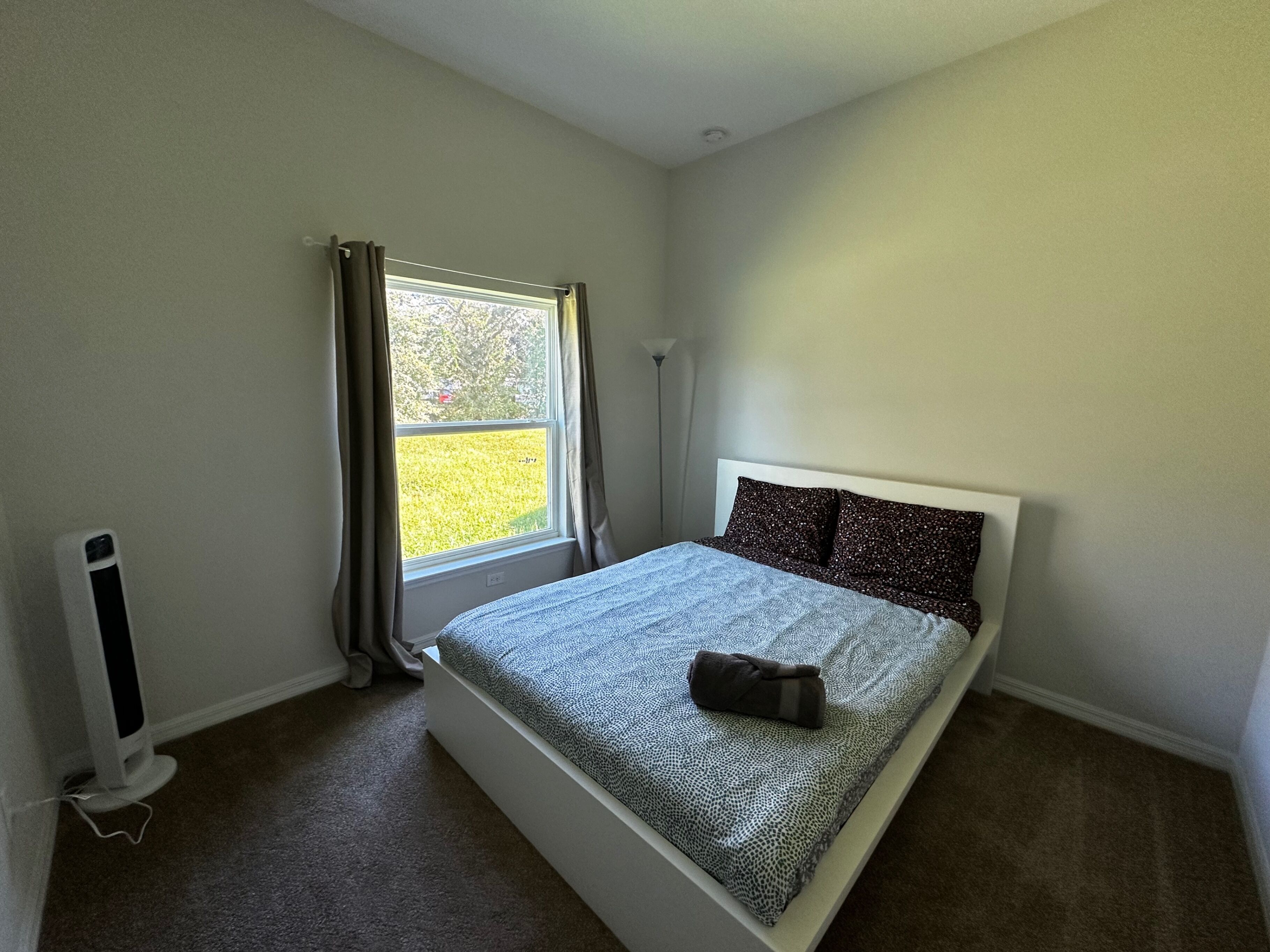 A bedroom with a bed, a window with curtains, a radiator, and a floor lamp.