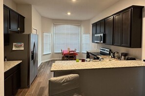 A modern kitchen with dark cabinets, a central island, and a dining area with a red table and chairs. - Beautiful House Close to Attractions and Amenities (Kissimmee)