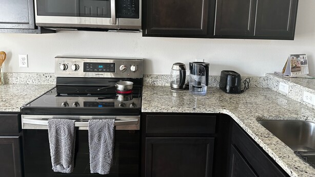 Eine Küche mit Mikrowelle aus Edelstahl, einem Herd von Samsung, einer Kaffeemaschine und einem Toaster.