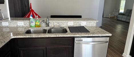A kitchen with a stainless steel dishwasher, a granite countertop, and a black cabinet.