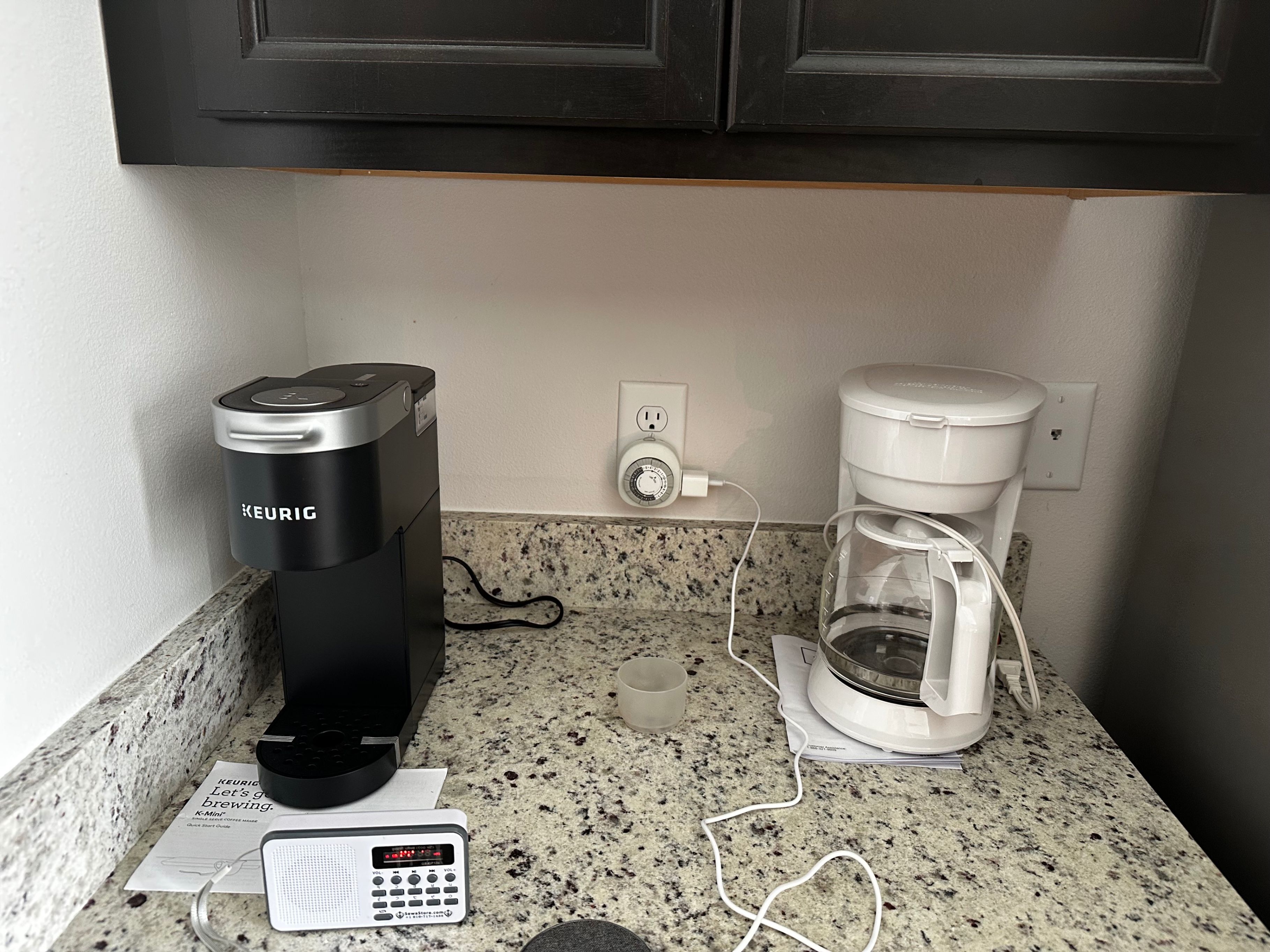 Une machine à café posée sur un plan de travail en granit, avec une minuterie et une cafetière.
