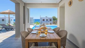 A dining table with breakfast items, wicker chairs, and a view of a swimming pool and buildings.