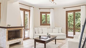 Una sala de estar con chimenea, un sofá, una mesa de centro y ventanas grandes con cortinas.