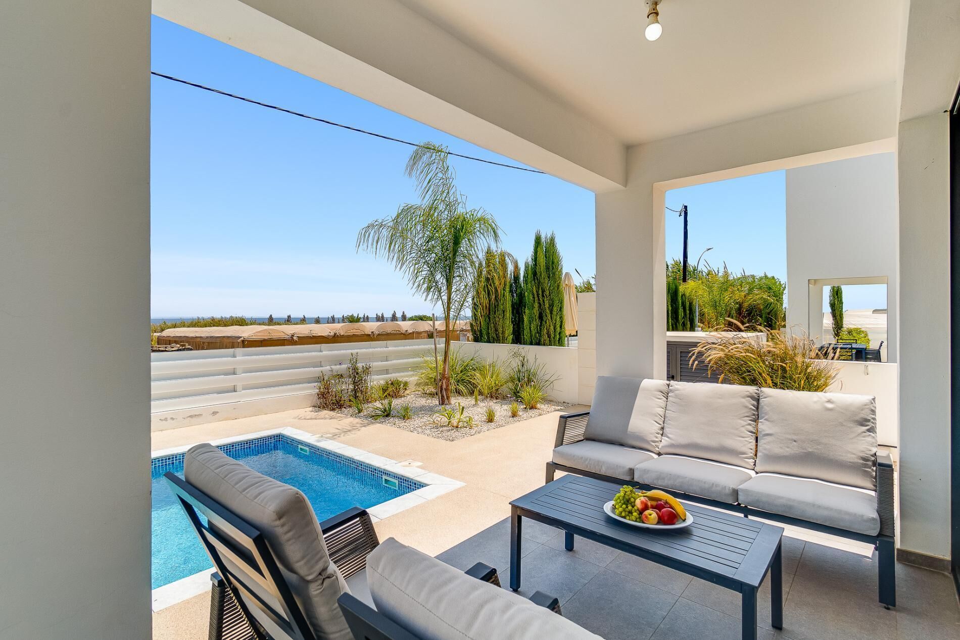 A balcony with a pool, seating, and a view of the beach.