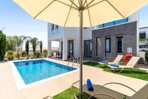 Ein Swimmingpool mit Liegestühlen und Sonnenschirm, umgeben von einem modernen Gebäude mit Poolbereich.