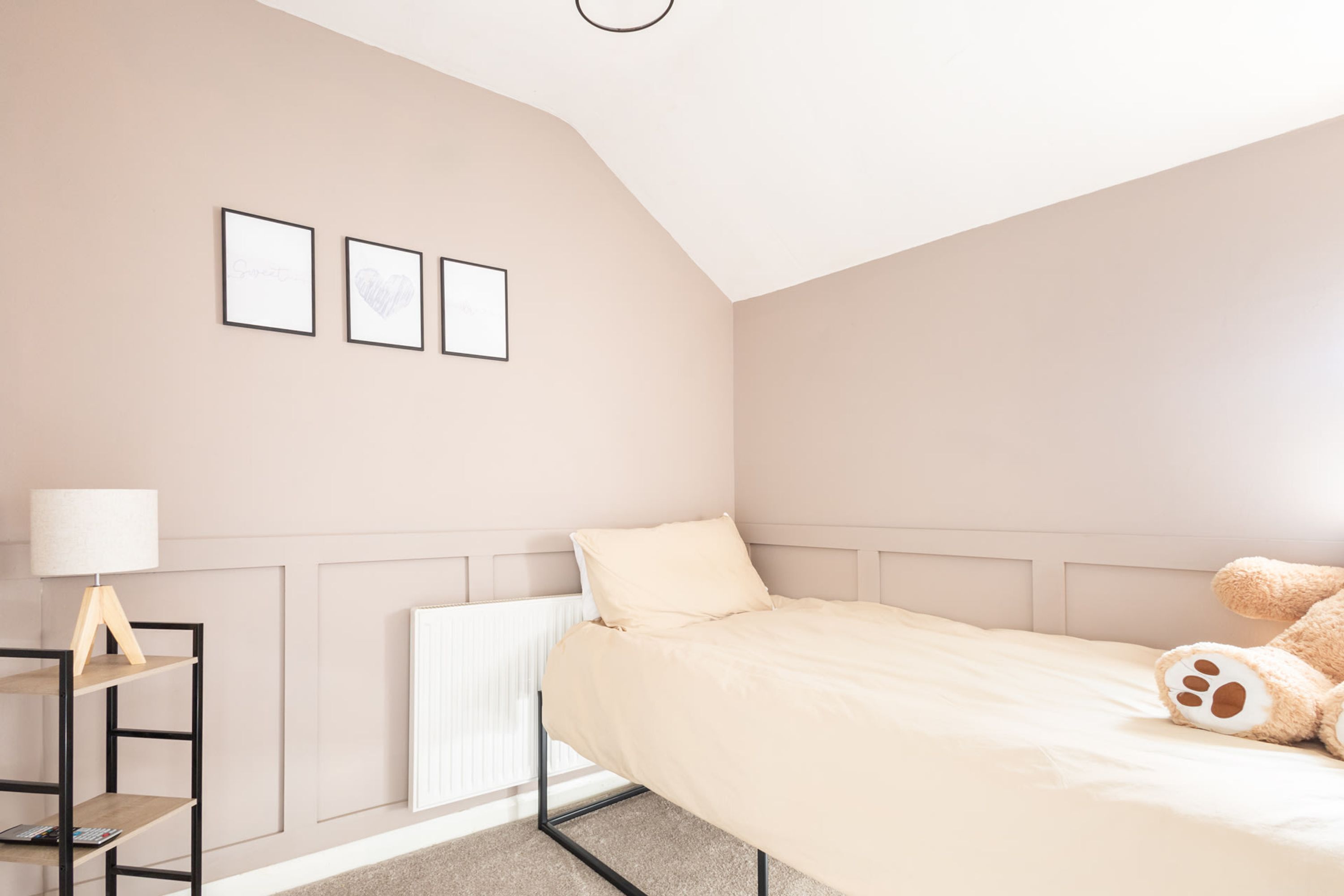 A bedroom with a bed, a lamp, a shelf, and three framed pictures on the wall.