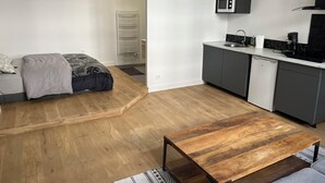 A modern apartment with a wooden floor, a grey sofa, a wooden coffee table, a kitchen with grey cabinets, a microwave, and a built-in oven. - Casa Baïona  (Bayonne)