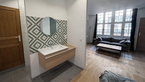 A modern apartment with a wooden door, a bathroom with a patterned backsplash, a sofa, and a large window. - Casa Baïona  (Bayonne)