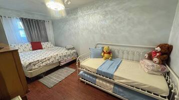 Une chambre avec deux lits, une commode en bois et un luminaire fixé au plafond.