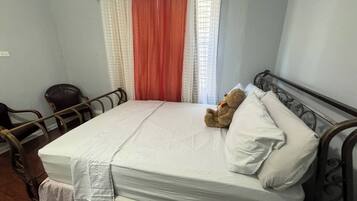 A single-bed room with a mattress, pillows, a teddy bear, a chair, and curtains.