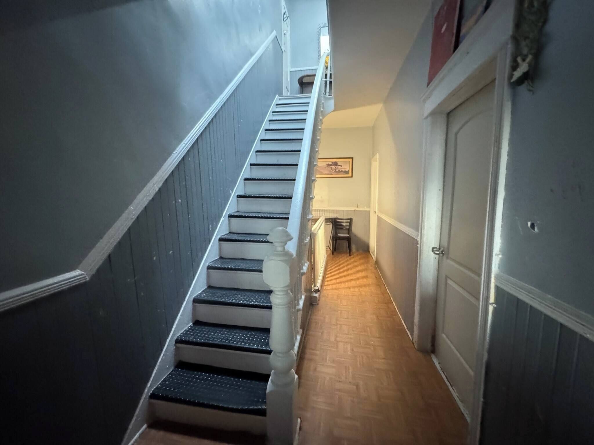 Uma escadaria com corrimão, uma cadeira e uma porta no final.